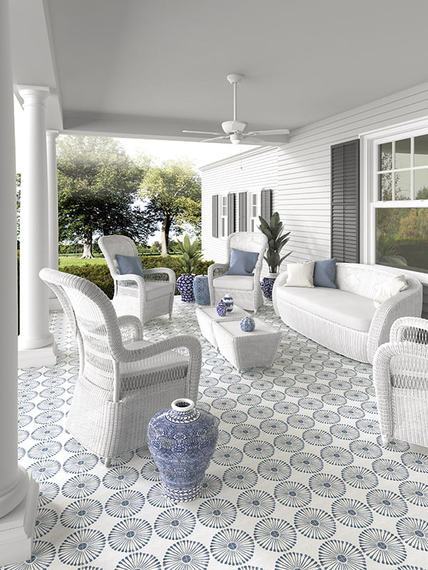 A cottage core patio on a white house, with white furnishings and our miramar 8x8 flower burst pattern tiles on the floor. there are navy accents to compliment the tiles blue and grey colour. 