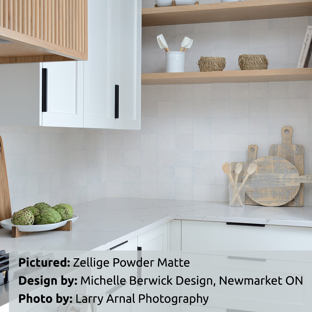 A modern neutral white kitchen with light wood shelves and accents, and warm zellige powder matte textured handmade look tiles installed on the backsplash. 