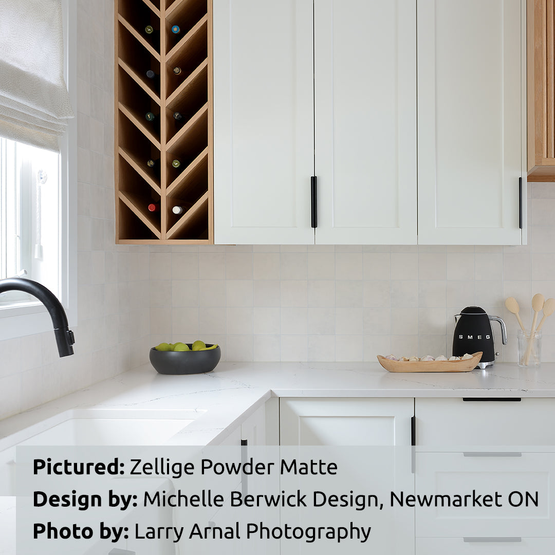 A modern white kitchen with light wood accents, and zellige powder matte textured handmade look tiles installed on the backsplash. 